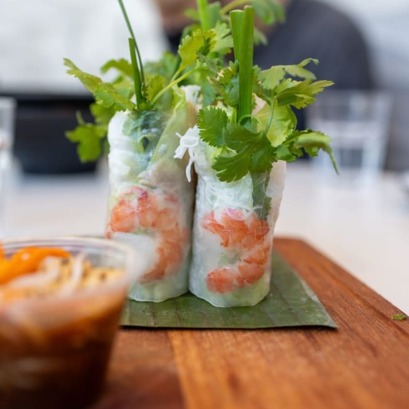 Two fresh Vietnamese spring rolls with shrimp and herbs on a banana leaf, with dipping sauce.