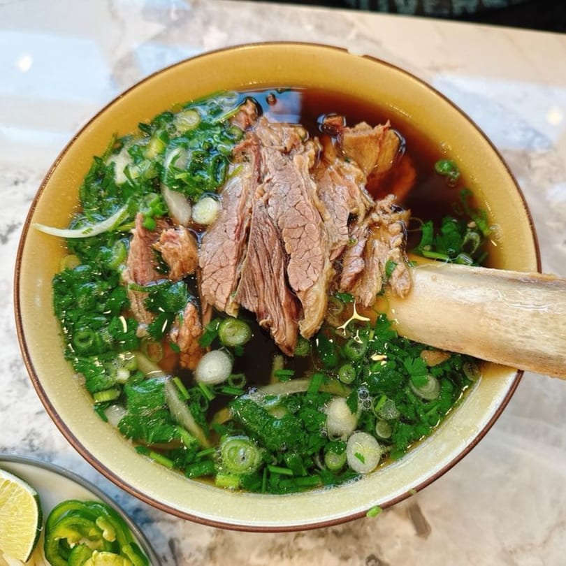 A bowl of PHO 408 pho with beef, green onions, and cilantro, with a bone in the broth.
