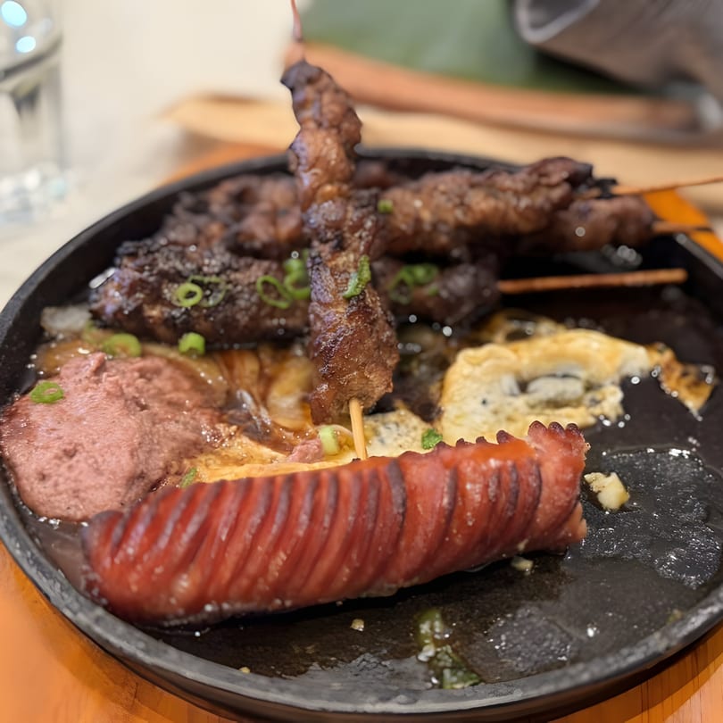 Sizzling platter with grilled meats on skewers, sausage, and other Vietnamese dishes.
