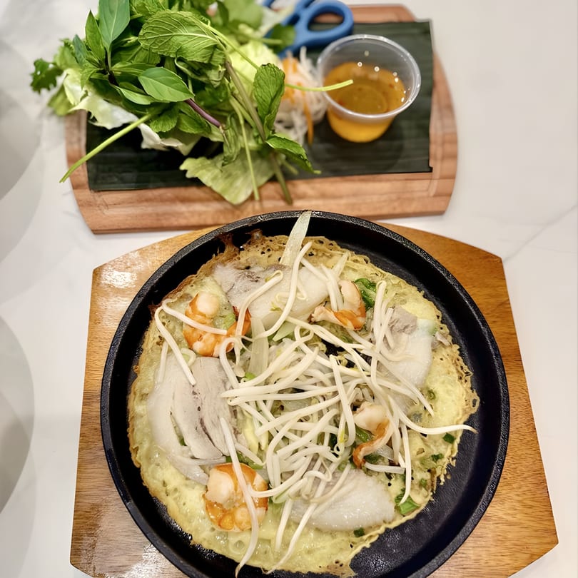 Vietnamese sizzling crepe with shrimp, pork, and bean sprouts, served with fresh herbs and dipping sauce.
