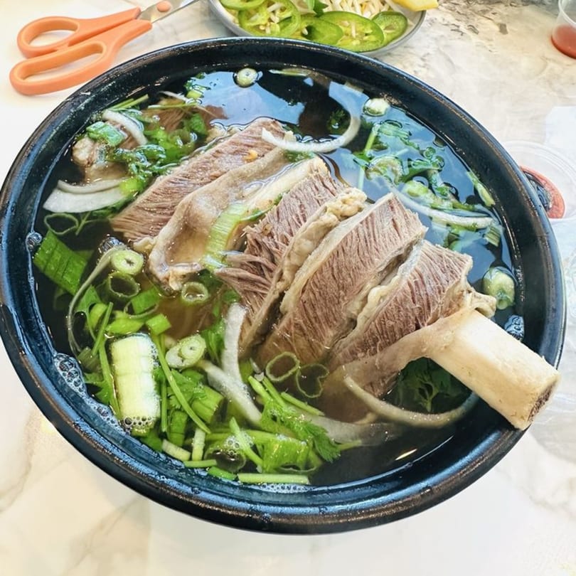 A close-up of a large bowl of PHO 408 pho with sliced beef, bone marrow, and fresh herbs.