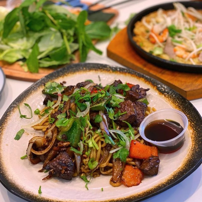Vietnamese stir-fried noodles with beef, vegetables, and a side of sauce on a plate.